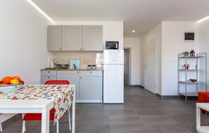 Eine moderne Küche mit weißen Schränken, einer eingebauten Mikrowelle und einem Kühlschrank. Ein Esstisch mit farbigem Tischlein und roten Stühlen steht im Raum.