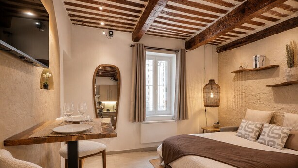 Ein Schlafzimmer mit einem Bett, einem Holztisch mit Stühlen, einem Spiegel, einem Fenster mit Vorhängen und einem Regal mit Büchern und einer Lampe.