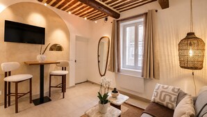 Ein modernes Wohnzimmer mit einer Couch, zwei Sesseln, einem kleinen Tisch, einem an der Wand montierten Fernseher und einem Fenster mit Vorhängen.