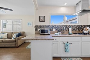 A modern kitchen with a microwave, sink, and stove, a white countertop, and a view of the outside. - The Tidal Retreat- Ocean Views (San Diego)