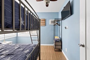 Ein Schlafzimmer mit Etagenbetten, einem kleinen Tisch, einem an der Wand montierten Fernseher und einem Regal mit gefalteter Kleidung.