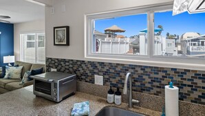A kitchen with a toaster, a sink, and a window with a view of a white fence and umbrellas. - The Tidal Retreat- Ocean Views (San Diego)
