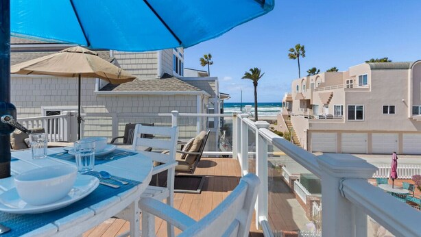 A balcony with a table set for two, overlooking the ocean and neighboring buildings. - The Tidal Retreat- Ocean Views (San Diego)