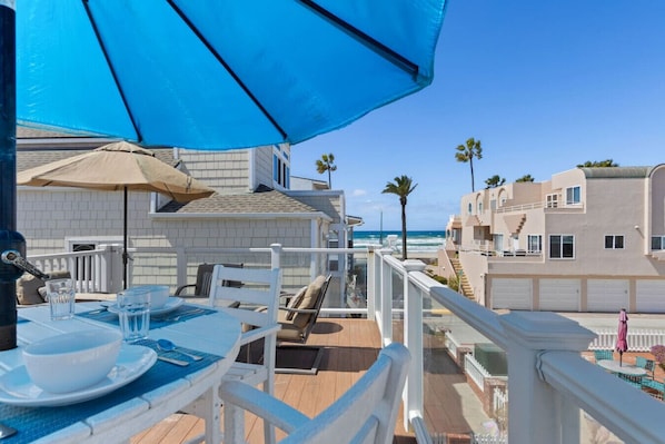 A balcony with a table set for two, overlooking the ocean and neighboring buildings. - The Tidal Retreat- Ocean Views (San Diego)