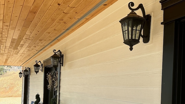 A covered outdoor seating area with wicker furniture and black wall-mounted lamps. - Romantic 1-bedroom 2 bath french farmhouse with a polish of a high end hotel. (Three Rivers)