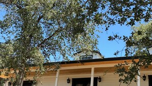 A two-story house with a covered porch, a visible chimney, and a large tree in the foreground. - Romantic 1-bedroom 2 bath french farmhouse with a polish of a high end hotel. (Three Rivers)