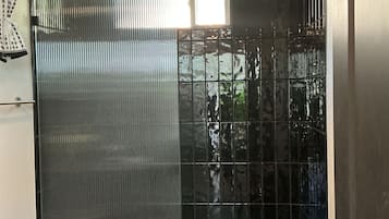 A modern bathroom with a toilet, a shower area with a glass door, and a small window providing natural light.