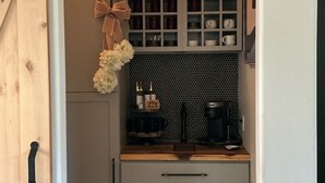 A kitchen with a sliding door, cabinets, a coffee maker, and a decorative bow. - Romantic 1-bedroom 2 bath french farmhouse with a polish of a high end hotel. (Three Rivers)