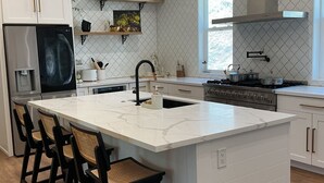 A modern kitchen with a central island, bar stools, white cabinetry, and a stainless steel refrigerator. - Romantic 1-bedroom 2 bath french farmhouse with a polish of a high end hotel. (Three Rivers)