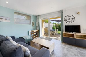 A modern living room with a sofa, coffee table, TV, and sliding glass doors leading to an outdoor patio. - Gite la Dune 3 km from the Beaches (Telgruc-sur-Mer)