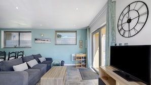 Un salon moderne avec un canapé gris, une table basse en bois et un grand téléviseur à écran plat posé sur un meuble en bois.