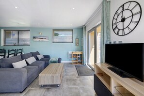 Ein modernes Wohnzimmer mit einer grauen Couch, einem Holztisch und einem großen Flachbildfernseher auf einem Holzständer.