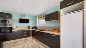 Une cuisine moderne dotée d’un four à micro-ondes, d’un four et d’un évier encastrés, avec des meubles de rangement de couleur sombre et un plan de travail clair.