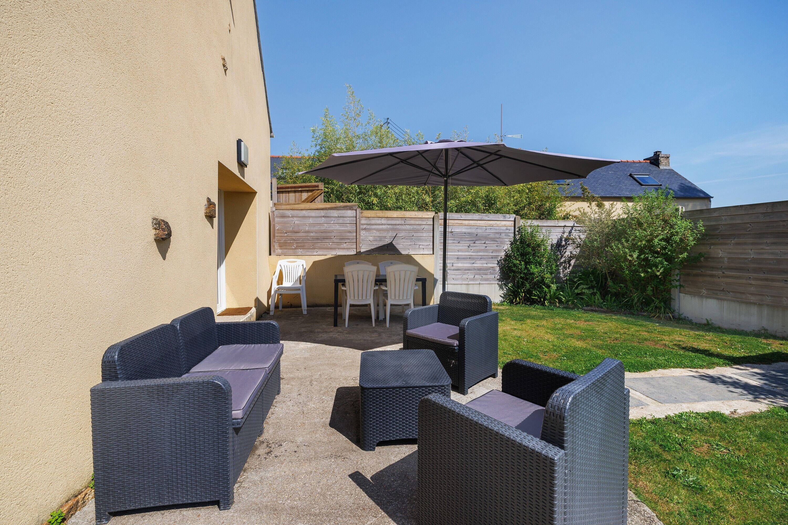 Une terrasse extérieure aménagée avec des meubles en osier, une table, des chaises et un grand parasol.