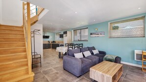 Un salon moderne avec un escalier en bois, un canapé, une table basse et une cuisine en arrière-plan.