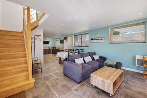Ein modernes Wohnzimmer mit einer Holztreppe, einer Couch, einem Couchtisch und einer Küche im Hintergrund.