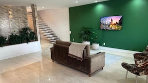 Un área de estar moderna con un sofá, una silla, una escalera y una pared verde con un televisor.