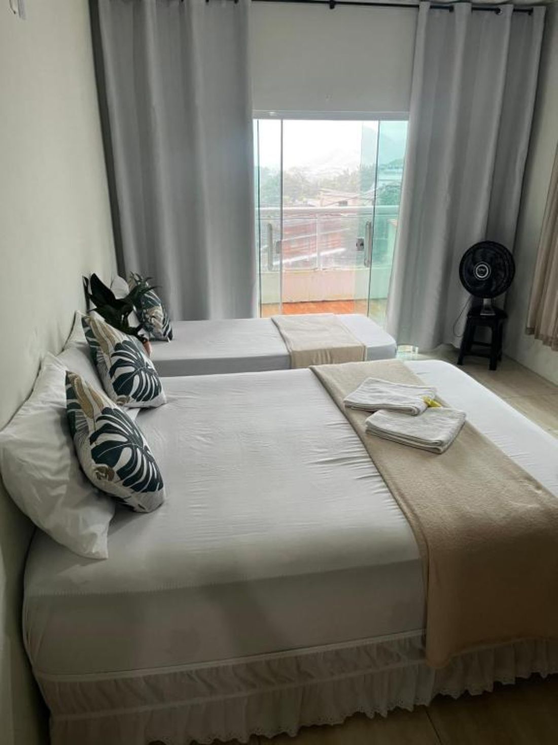 Quarto de hotel com duas camas, varanda e ventilador.