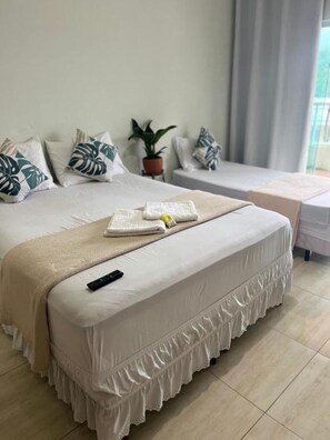 Una cama bien hecha, con un control remoto, una planta en maceta y una mesita de noche con lámpara.