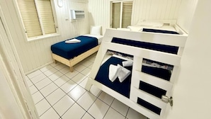 Ein Zimmer mit zwei Betten, eines mit blauer und das andere mit weißer Matratze. Über den Betten befindet sich eine weiße Wand-Klimaanlage.