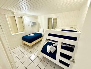 Huoneessa on kaksi sänkyä, toisessa on sininen patja ja toisessa valkoinen. Sänkyjen yläpuolella seinälle on asennettu valkoinen ilmastointilaite.