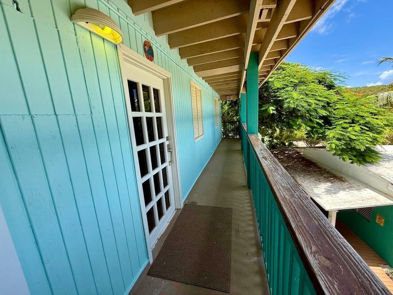 Un porche cubierto con puerta y ventanas, un banco de madera y vistas al follaje.
