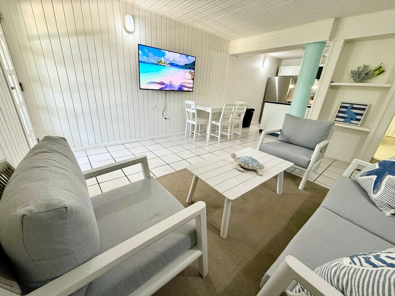 Una sala de estar con televisor, sofás grises, una mesa de centro y un comedor con sillas.