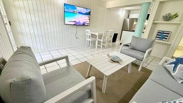 Una sala de estar con televisor, sofás grises, una mesa de centro y un comedor con sillas.