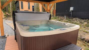 A hot tub with a wooden deck, a covered area, and a building in the background.