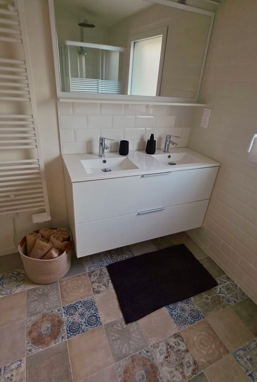 A bathroom with a white vanity, two sinks, a mirror, and a towel basket.