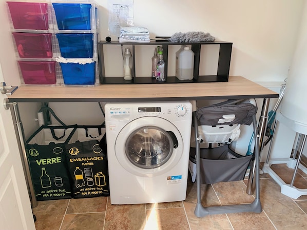 A laundry area with a washing machine, storage bins, and cleaning supplies.