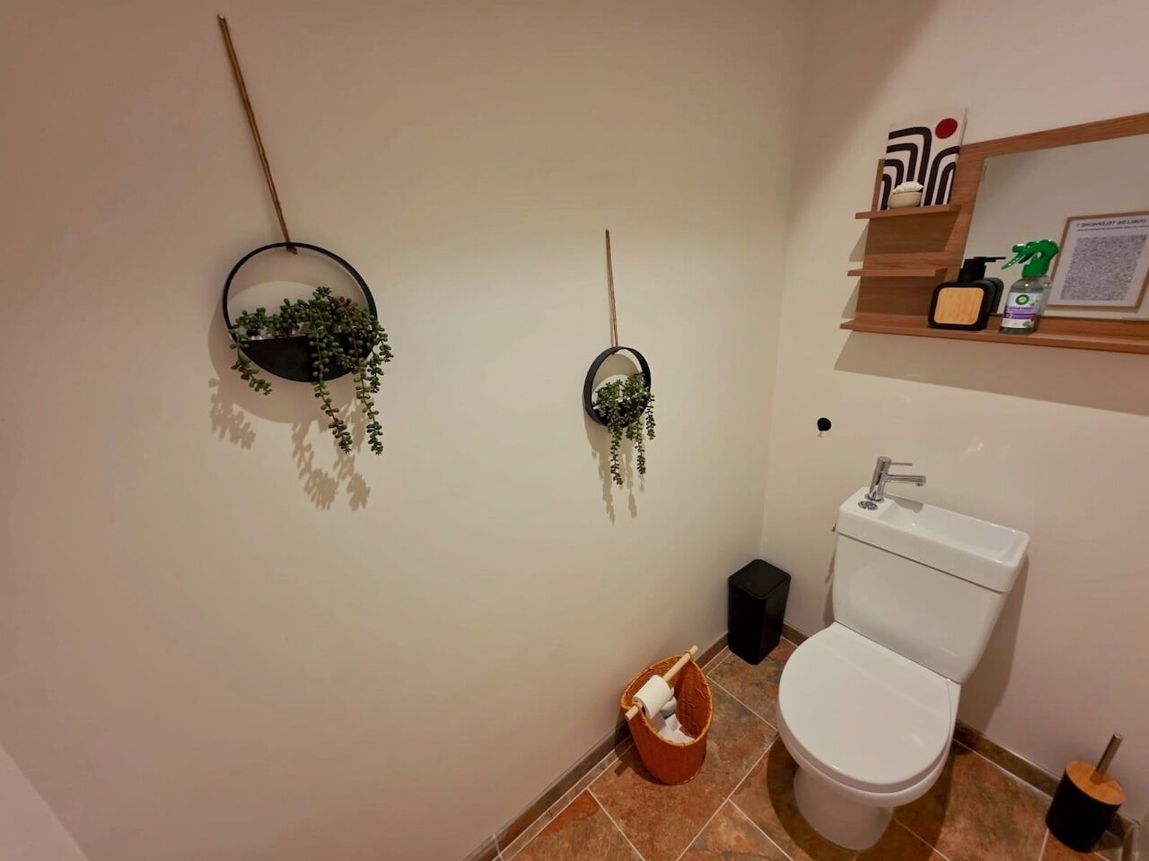 Une salle de bain équipée de toilettes, d’un lavabo et de deux plantes fixées au mur.