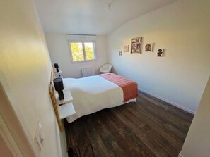Een slaapkamer met een bed, een raam, een radiator, een witte stoel en wanddecoratie.