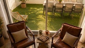 Two leather chairs with cushions, a wooden table with a chessboard, and a view of a patio with a table and chairs. - Large house for 7 people on the outskirts of Brocéliande (Campénéac)