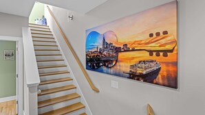 Una escalera de madera con barandilla blanca que conduce a una habitación con un cuadro grande de un paisaje urbano en la pared.