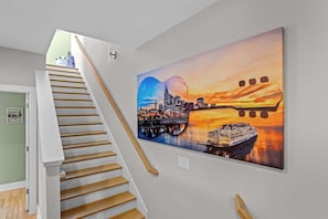 A staircase with wooden steps and a white handrail, leading to a room with a large cityscape painting on the wall. - Sounds Like Fun- Hot Tub, Firepit, Mini Golf & Skyline Views, Near Broadway (Nashville)