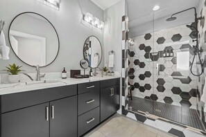 A modern bathroom with a large mirror, a shower with a glass door, and a hexagonal tile backsplash. - Sounds Like Fun- Hot Tub, Firepit, Mini Golf & Skyline Views, Near Broadway (Nashville)