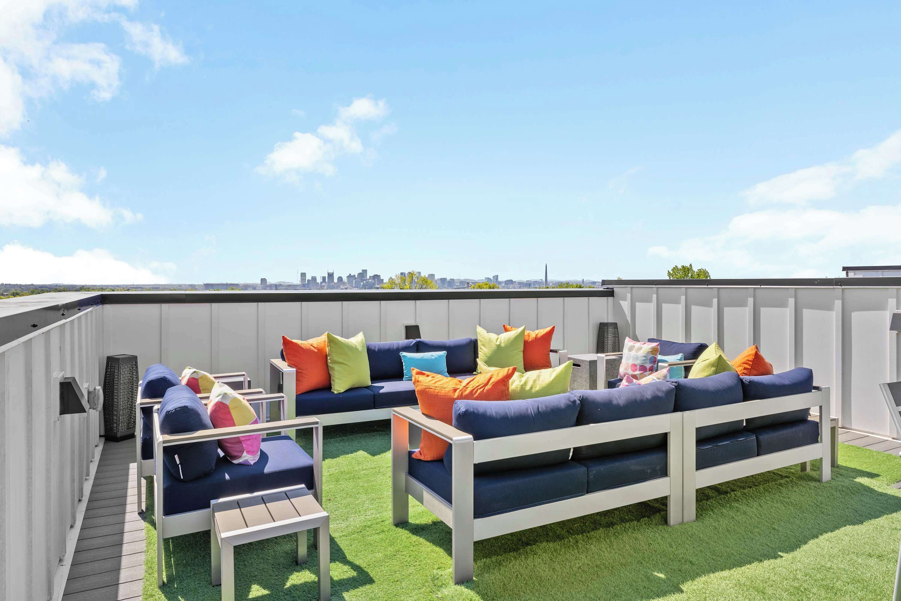 A rooftop patio with a sectional sofa, a small table, and a view of the city skyline.