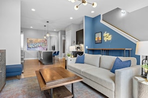 A modern living room with a sofa, coffee table, and a kitchen in the background. - Sounds Like Fun- Hot Tub, Firepit, Mini Golf & Skyline Views, Near Broadway (Nashville)