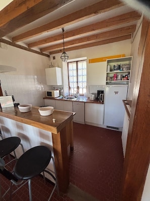 A kitchen with a wooden island, white cabinets, a refrigerator, and a window with curtains. - Étang du Sanglier Vacation Rental (Paulnay)