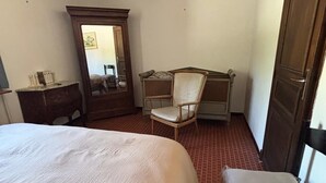 Een slaapkamer met een groot bed, een stoel, een tafeltje, een spiegel en een kledingkast.