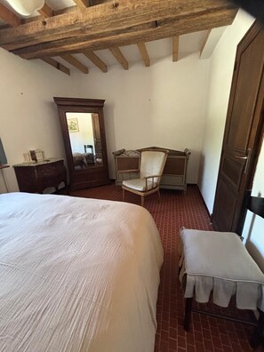 A bedroom with a large bed, a chair, a small table, a mirror, and a wardrobe. - Étang du Sanglier Vacation Rental (Paulnay)