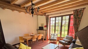 Een woonkamer met een bank, salontafel en stoelen. Er is een eettafel met stoelen, een televisie en een raam met gordijnen.