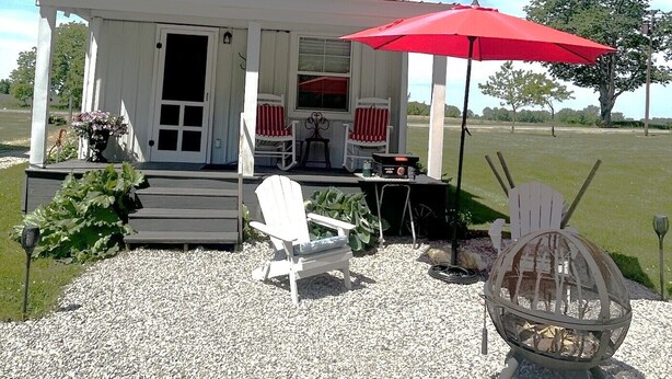 A house with a porch, two rocking chairs, a red umbrella, and a fire pit. - Cottage in Bancroft countryside for the perfect relaxing getaway. (Bancroft)