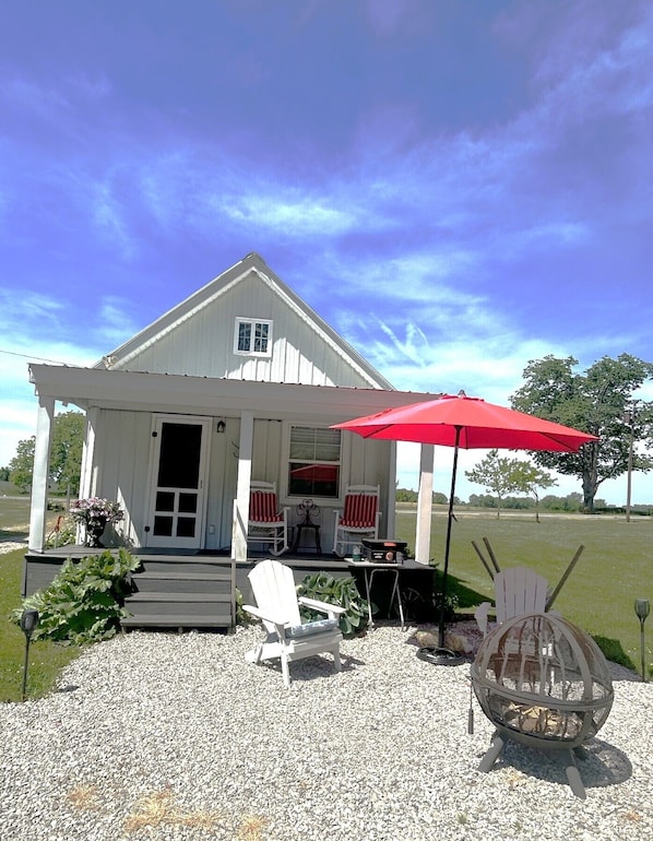Une maison avec une véranda, deux fauteuils à bascule, un parasol rouge et un foyer extérieur.