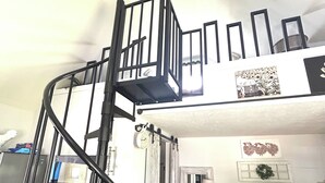 A bunk bed room with a staircase, a fan, a clock, a framed picture, a mirror, a bedside table with a lamp, and a 'HELLO' pillow. - Cottage in Bancroft countryside for the perfect relaxing getaway. (Bancroft)