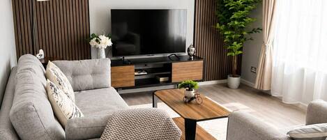 A modern living room with a sofa, coffee table, TV, and decorative plants.