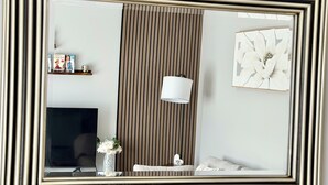 Una habitación con televisión, lámpara, un florero con flores, un cuadro enmarcado y pared a rayas.