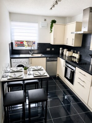 A modern kitchen with a dining area, black tiled flooring, and a window with blinds. - Modern Central Aberdeen 2BR Apartment with Parking | Business & Leisure (Aberdeen)