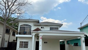 A two-story building with a covered parking area, a balcony with chairs, and a large window.